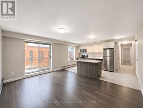 St. Catharines (Downtown) multi-family for rent - A spacious, empty room with a kitchenette and a refrigerator.