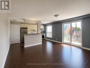 St. Catharines (Downtown) multi-family for rent - A spacious living room with hardwood floors and a kitchen area in the background.