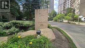 Mississauga (City Centre) condo for rent - A stone monument with the word "OATION" engraved on it is surrounded by greenery.