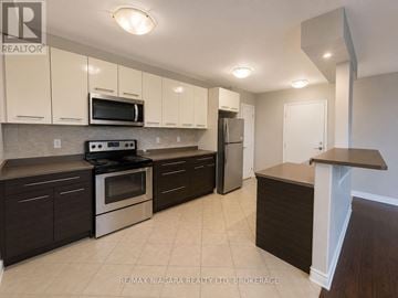 St. Catharines (Downtown) multi-family for rent - A kitchen with a stove top oven, microwave, refrigerator, and cabinets.
