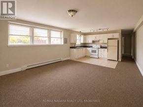 St. Catharines (E. Chester) multi-family for rent - A spacious empty room with a kitchenette in the background.