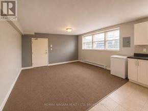 St. Catharines (E. Chester) multi-family for rent - A room with a brown carpet and a white refrigerator.