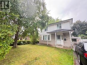 Brampton (Madoc) apartment for rent - A house with a grey roof and white walls is surrounded by greenery.