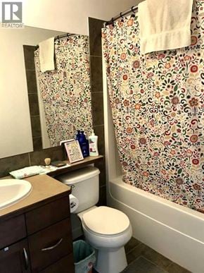 Lethbridge apartment for rent - A bathroom with a toilet, sink, and floral shower curtain.