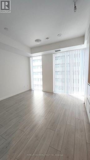 Toronto (Waterfront Communities) condo for rent - A spacious room with wooden flooring and a large window with blinds.