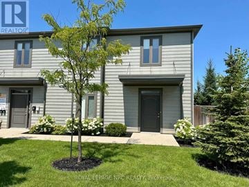 St. Catharines (Oakdale) apartment for rent - A tree in a flower bed in front of a grey house.