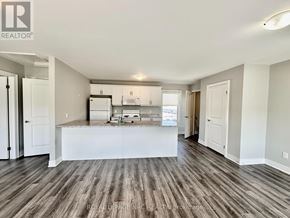 St. Catharines (Oakdale) apartment for rent - A spacious room with wooden flooring and a kitchen area in the background.