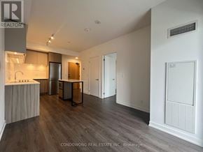 Vaughan (Beverley Glen) condo for rent - A spacious room with wood flooring and a kitchen area with a refrigerator, sink, and cabinets.