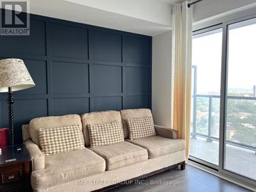 Toronto (Cabbagetown-South St. James Town) condo for rent - A living room with a beige couch and a lamp on a side table.