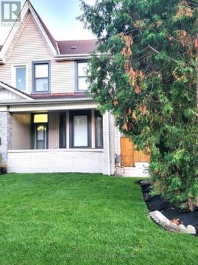 Toronto (Junction Area) duplex for rent - A house with a well-kept lawn and a tree with orange leaves.