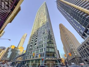 Toronto (Waterfront Communities) condo for rent - A tall, modern glass building stands in the middle of a bustling city street.