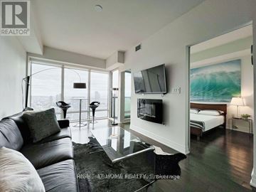 Toronto (Waterfront Communities) condo for rent - A living room with a black leather couch and a flat screen TV mounted on the wall.