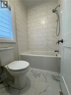 Kitchener apartment for rent - A white toilet sits in a bathroom with a marble floor and white tiles.