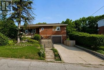 Niagara Falls (Downtown) fourplex for rent - A house with a brown brick exterior and a white window is surrounded by greenery.