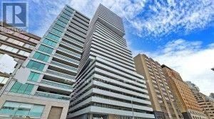 Toronto (Annex) condo for rent - A tall building with many windows is under a blue sky.