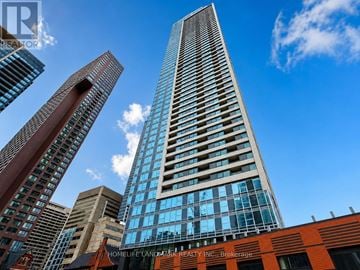 Toronto (North St. James Town) condo for rent - A tall building with a glass facade stands in front of other buildings on a sunny day.