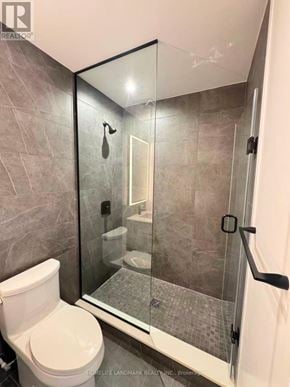 Toronto (North St. James Town) condo for rent - A bathroom with a toilet, a walk-in shower, and a glass door.