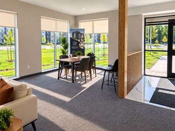 Dieppe apartment for rent - A modern living room with a dining table and chairs, a sofa, and a view of a green outdoor area through large windows.