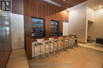 Toronto (Waterfront Communities) condo for rent - A bar area with stools and a refrigerator in a modern kitchen.