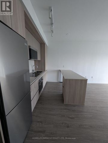 Mississauga (Central Erin Mills) condo for rent - A kitchen with a refrigerator, microwave, and wooden cabinets.