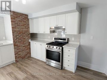 Toronto (Palmerston-Little Italy) multi-family for rent - A kitchen with white cabinets and a brick wall.