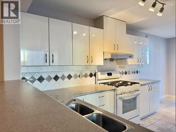 Burnaby apartment for rent - A kitchen with white cabinets and a black and white tiled backsplash.