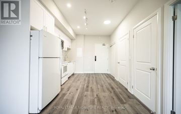 St. Catharines (E. Chester) condo for rent - A white refrigerator is in the middle of a kitchen with wooden floors and white walls.