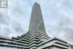 Toronto (Mimico) condo for rent - A tall building with a unique curved design stands against a cloudy sky.