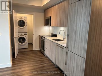 Mississauga (City Centre) condo for rent - A modern kitchen with wooden cabinets and a washer and dryer built in.