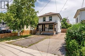 Niagara Falls (Downtown) apartment for rent - A two-story house with a front porch is surrounded by a wooden fence and has a tree in the front yard.