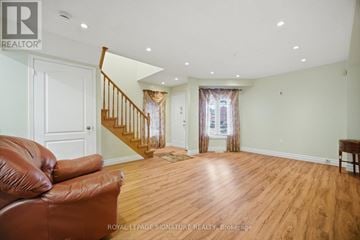 Brampton (Sandringham-Wellington) apartment for rent - A brown leather couch sits in a spacious living room with wood floors and white walls.