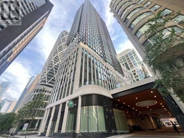 Toronto (University) condo for rent - A tall building with a glass facade stands in front of other buildings.