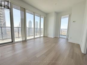 Toronto (Mimico) condo for rent - A spacious room with wooden flooring and large windows overlooking a cityscape.