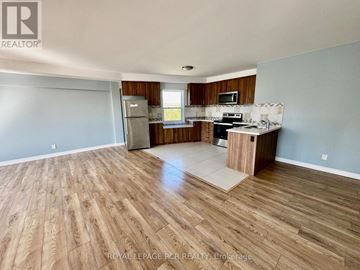 Orangeville multi-family for rent - A spacious room with wooden flooring and a kitchen area with a refrigerator, microwave, and oven.