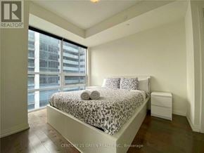 Toronto (Moss Park) condo for rent - A bedroom with a large bed and a window overlooking a cityscape.