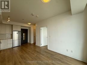Toronto (Henry Farm) condo for rent - A spacious room with wood flooring and white walls, featuring a kitchen area with a refrigerator and cabinets.