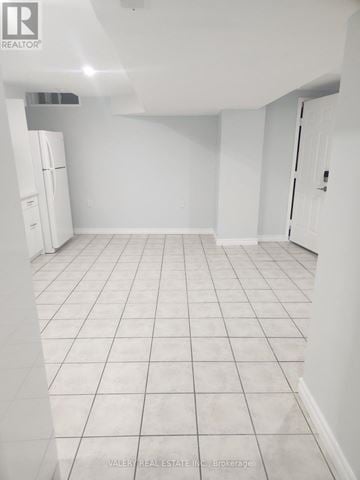 Ajax (Central West) apartment for rent - A white tiled kitchen with a refrigerator and a door on the right.