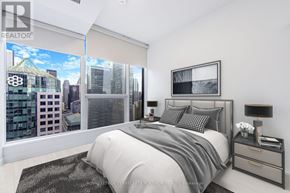 Toronto (Waterfront Communities) condo for rent - A bedroom with a large bed, a nightstand, and a window overlooking a cityscape.