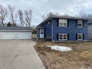 Grand Forks apartment for rent - A blue house with a white garage door and a small tree in front.