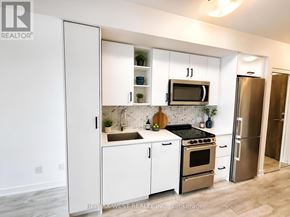 Toronto (Mimico) condo for rent - A kitchen with white cabinets and appliances, a sink, and a refrigerator.
