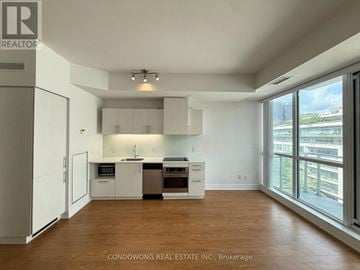 Toronto (Waterfront Communities) condo for rent - A spacious kitchen with white cabinets and appliances, hardwood floors, and a large window with a view of the city.