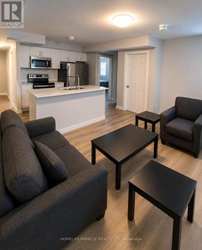 Barrie (Georgian Drive) townhouse for rent - A living room with a grey couch, a black coffee table and a kitchen area in the background.