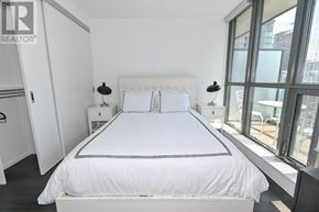 Toronto (Waterfront Communities) condo for rent - A bedroom with a large bed, two lamps, and a window overlooking a cityscape.