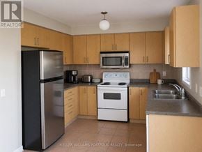 Toronto (Rouge) townhouse for rent - A kitchen with a black refrigerator, white stove, and wooden cabinets.