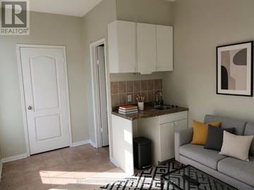 Toronto (Rouge) townhouse for rent - A living room with a grey couch and a kitchenette.