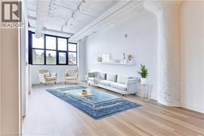 Guelph condo for rent - A living room with a white couch, a blue rug, and a window with a view of trees.