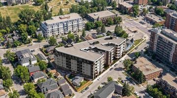 Calgary apartment for rent - A large building with a flat roof is surrounded by smaller buildings and trees.