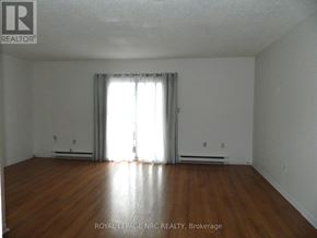St. Catharines (Carlton/Bunting) townhouse for rent - A room with wooden floors and white walls, with a window covered by white curtains.