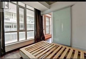 Toronto (Waterfront Communities) condo for rent - A bedroom with a bed, wooden headboard, and a window with a view of a building.