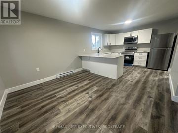 Gananoque triplex for rent - A kitchen with white cabinets and a wooden floor.